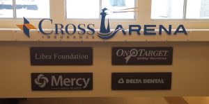 photo of cross insurance arena interior wall signage. Bronze backer panel with brushed aluminum logos. Clear acrylic backer with vinyl letter and logo